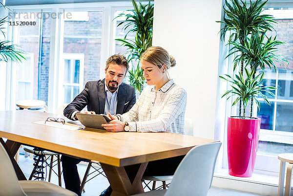 Geschäftsfrau und Mann schauen auf digitales Tablet bei Bürobesprechung