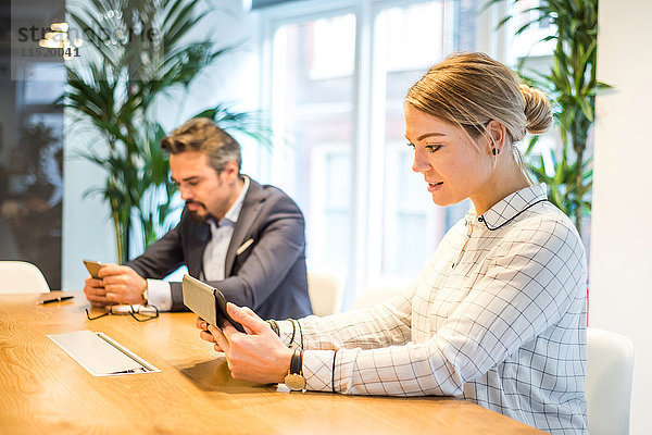 Geschäftsfrau und Mann am Büroschreibtisch mit Blick auf digitales Tablet und Smartphone