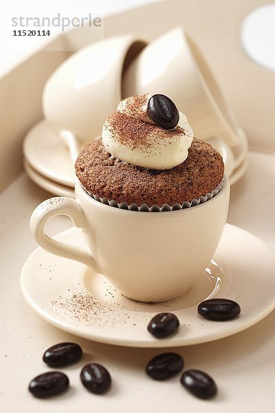Cupcakes mit Cappuccinogeschmack  Kaffeetassen und Schokoladenkaffeebohnen auf einem cremefarbenen Tablett