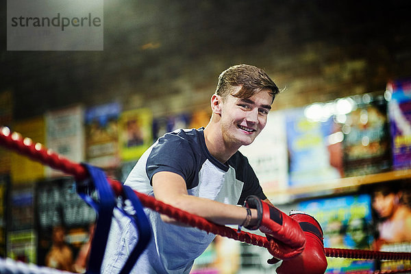 Porträt eines jungen männlichen Boxers  der sich an Boxring-Seile lehnt