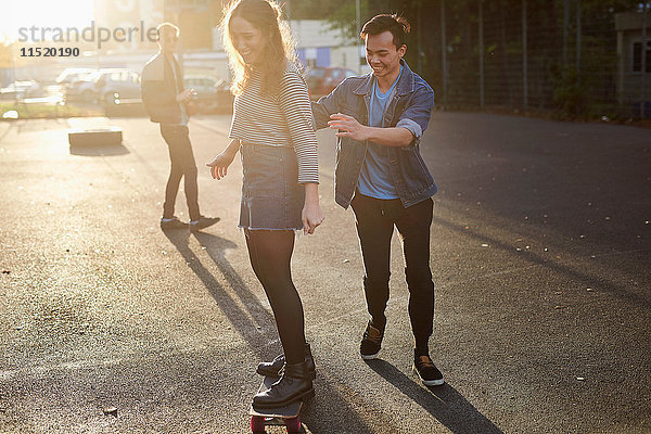 Junger Mann schiebt junge Skateboarderin auf sonnenbeschienener Straße