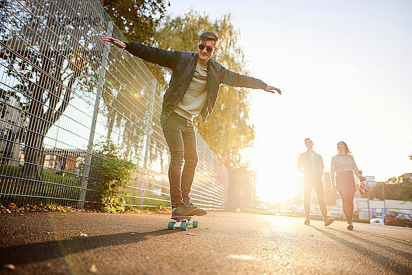 Junge männliche Skateboarder skateboarden auf sonnenbeschienener Strasse