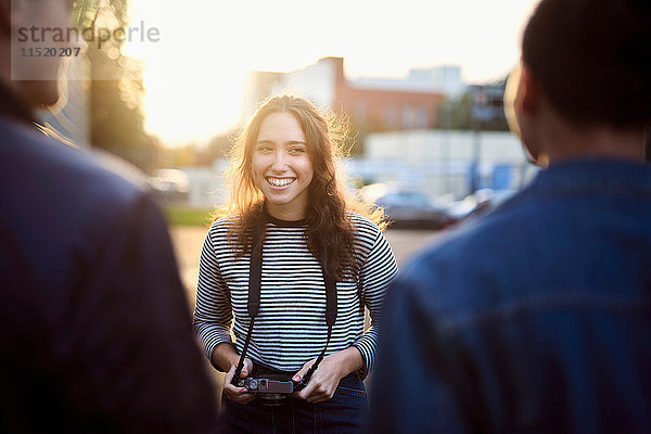 Über-Schulter-Ansicht einer jungen Frau im Gespräch mit männlichen Freunden auf einer sonnenbeschienenen Straße