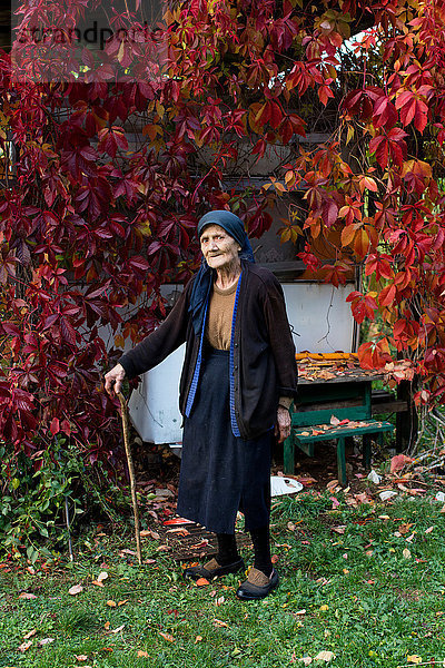 Porträt einer älteren Frau mit Spazierstock im Herbstgarten stehend