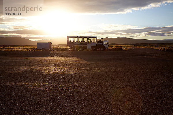 Touristen-Lkw bei Sonnenaufgang in einer Landschaft mit fernen Bergen geparkt  Island