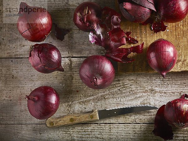 Rote Zwiebeln auf Schneidebrett und Holztisch mit Messer