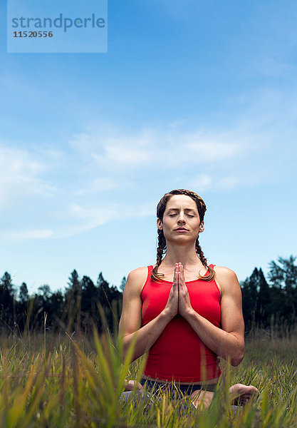 Junge Frau sitzt auf dem Feld  in Yogastellung