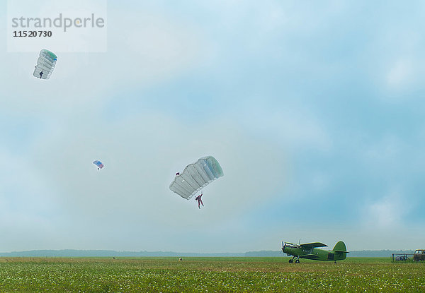 Distanzansicht von drei Personen  die mit einem Oldtimer-Flugzeug mit dem Fallschirm auf einen Flugplatz abspringen