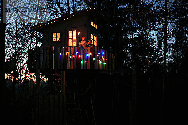 Junge mit Flammenfackel und sein Bruder blicken nachts vom Balkon des Baumhauses