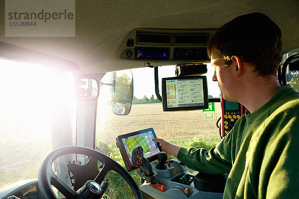 Junger Mann fährt Traktor mit Touchscreen am globalen Positionierungssystem