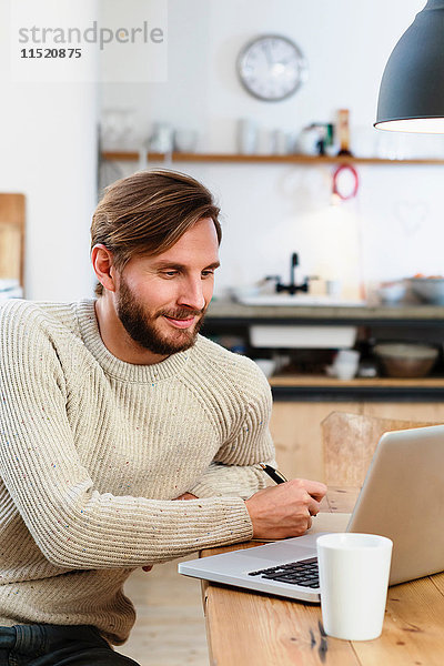 Mittelgroßer erwachsener Mann schaut auf Laptop auf dem Tisch