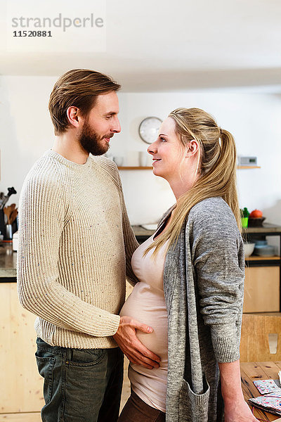 Mann berührt den Bauch der schwangeren Freundin in der Küche