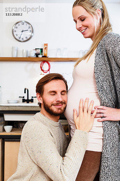 Mann berührt und hört den Bauch der schwangeren Freundin in der Küche