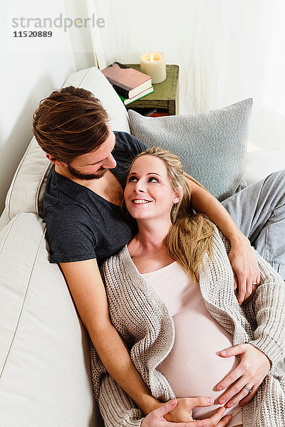 Schwangere Paare im mittleren Erwachsenenalter berühren schwangeren Bauch auf dem Sofa