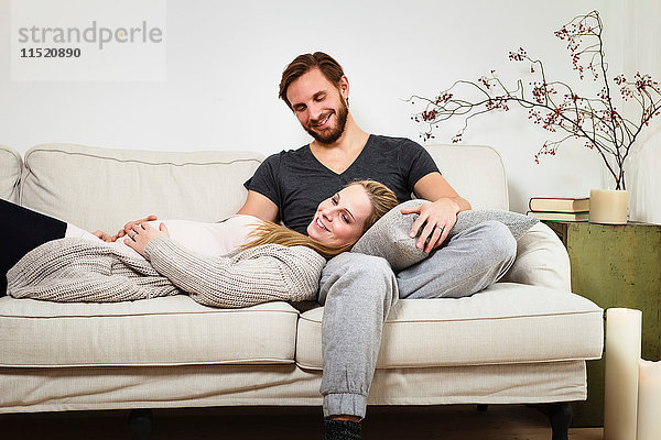 Schwangere Paare im mittleren Erwachsenenalter entspannen sich auf dem Sofa