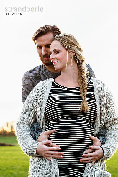 Mann umarmt und berührt den schwangeren Bauch seiner Freundin in Feldlandschaft
