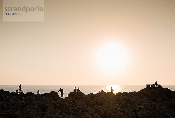 Silhouette von Menschen auf Felsen bei Sonnenuntergang  Ciutadella  Menorca  Spanien