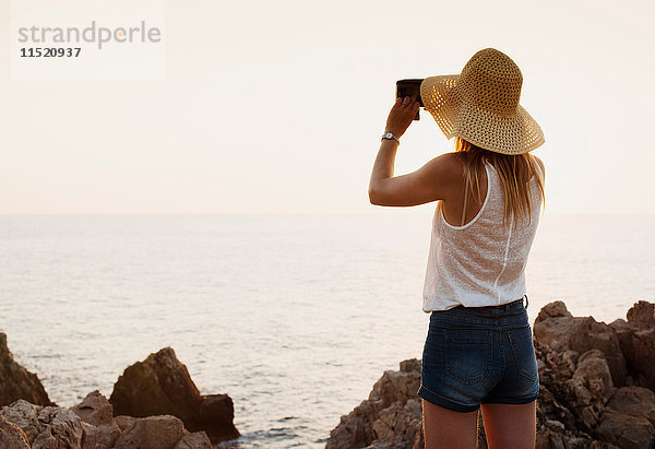 Rückansicht einer Frau  die mit einem Fernglas aufs Meer schaut  Ciutadella  Menorca  Spanien