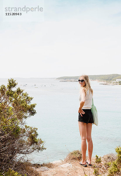 Frau am Meer schaut lächelnd über die Schulter in die Kamera  Menorca  Spanien