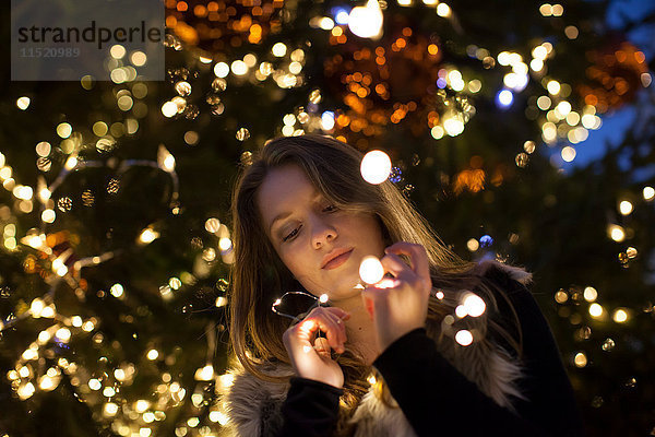 Junge Frau schaut auf Lichter in der Hand  Baum im Hintergrund