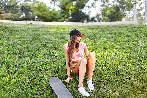 Junge Frau sitzt auf einem Grasrand  neben ihr ein Skateboard