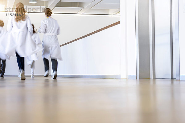 Rückansicht von männlichen und weiblichen Ärzten  die im Krankenhauskorridor laufen