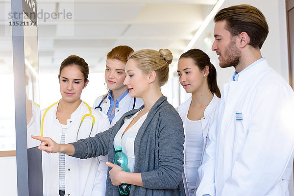 Frau mit männlichen und weiblichen Ärzten  die im Krankenhaus auf das Krankenblatt zeigen