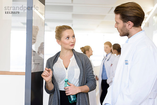 Frau und männlicher Arzt diskutieren im Krankenhauskorridor