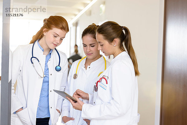 Drei junge Ärztinnen betrachten digitales Tablett im Krankenhauskorridor