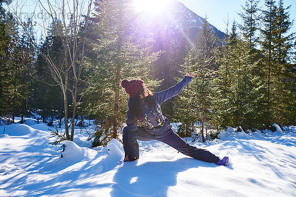 Frau in Winterkleidung praktiziert Yoga-Pose im Seitenwinkel im verschneiten Wald  Österreich