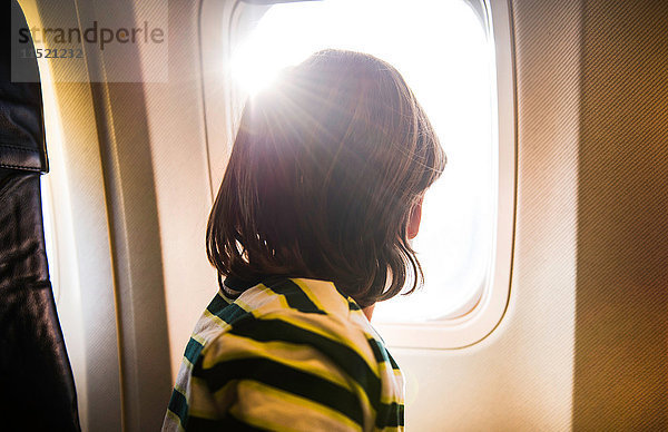 Junge im Flugzeug  der durch ein sonnenbeschienenes Flugzeugfenster schaut