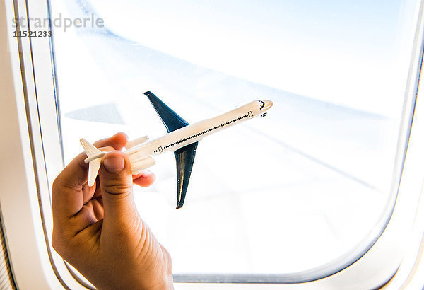 Hand eines Jungen spielt mit Spielzeugflugzeug am Flugzeugfenster