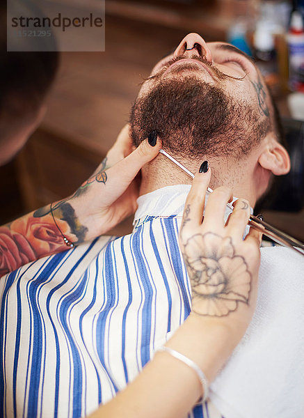 Friseur rasiert Bart des Kunden