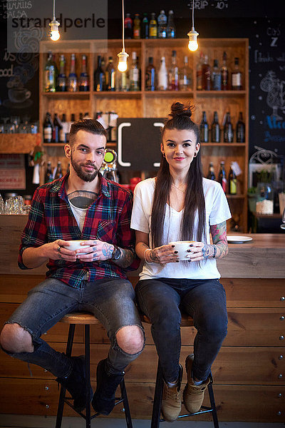 Paar sitzt nebeneinander auf Hockern im Café und schaut lächelnd in die Kamera
