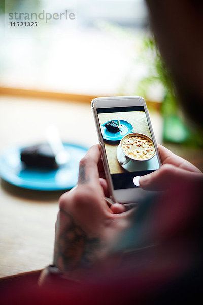 Mann fotografiert Kuchen auf heißer Schokolade mit einem Smartphone