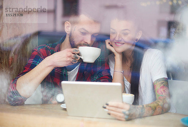 Blick durch das Fenster eines Paares im Café mit einem digitalen Tablett
