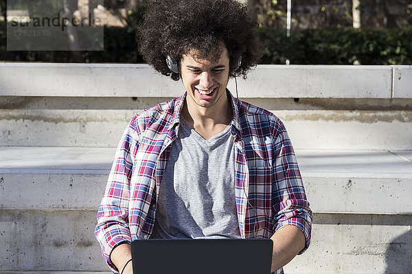 Lächelnder junger Mann mit Laptop und Kopfhörer