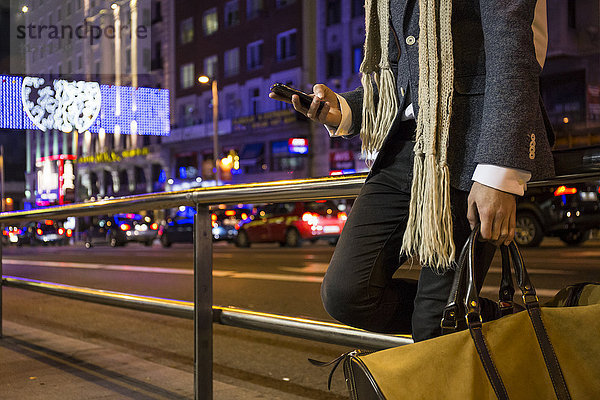 Ein Mann  der seine Tasche hält und sein Handy nachts in einer Straße benutzt.