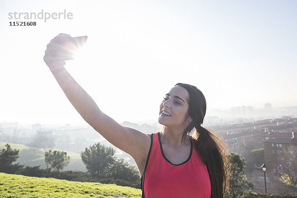 Lächelnde Sportlerin  die einen Selfie mit ihrem Handy nimmt.