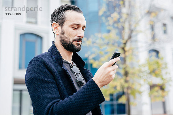 Mann auf der Straße mit Blick auf Mobiltelefon