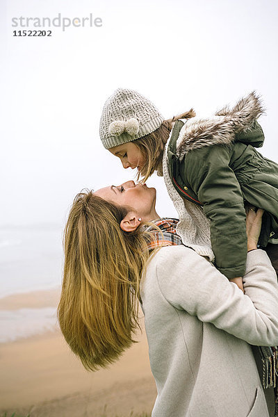 Frau beim Aufstehen und Küssen der Tochter am Strand im Winter