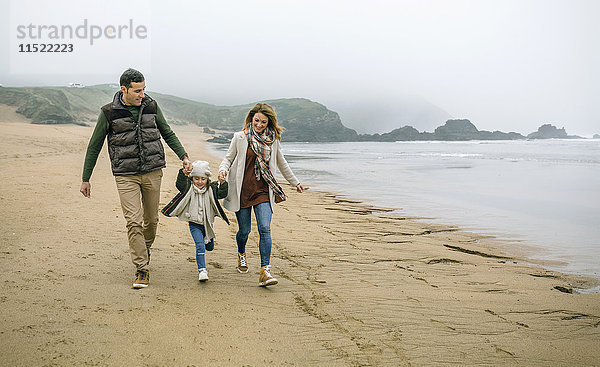 Glückliche Familie mit Tochter  die im Winter am Strand spazieren geht.