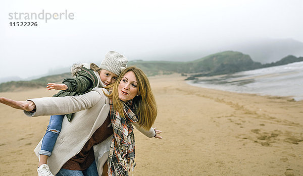 Glückliche Frau und Tochter tun so  als würden sie im Winter am Strand fliegen.