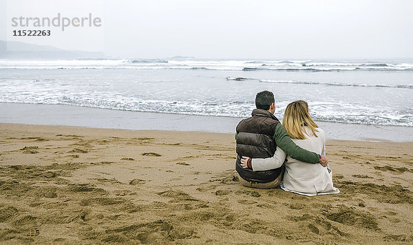 Verliebtes Paar im Winter am Strand sitzend