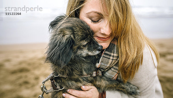 Frau umarmt ihren Hund am Strand im Winter