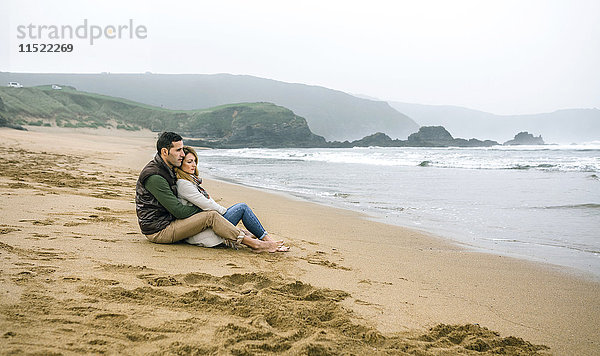 Verliebtes Paar im Winter am Strand sitzend