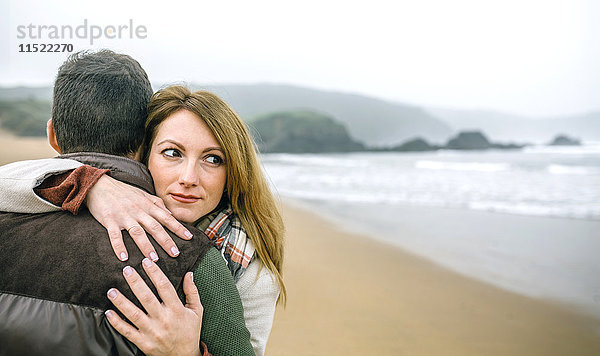 Frau umarmt Mann am Strand im Winter
