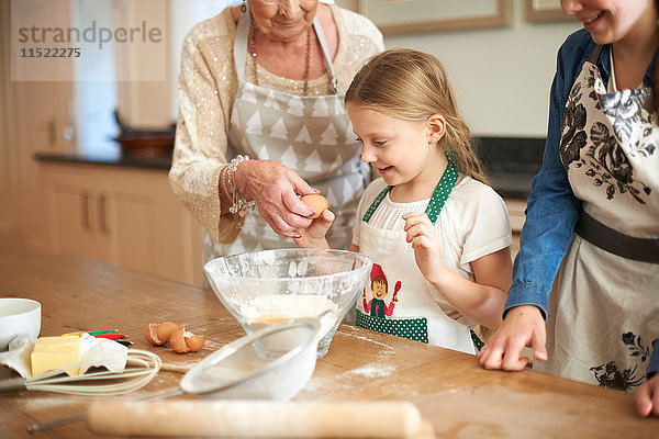Ältere Frau und Enkelinnen knacken Eier für Kekse