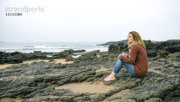 Einsame Frau sitzt im Winter auf Felsen am Strand.