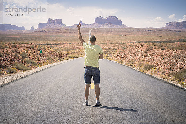 USA  Utah  Rückansicht des Mannes auf der Straße zum Monument Valley mit Siegeszeichen